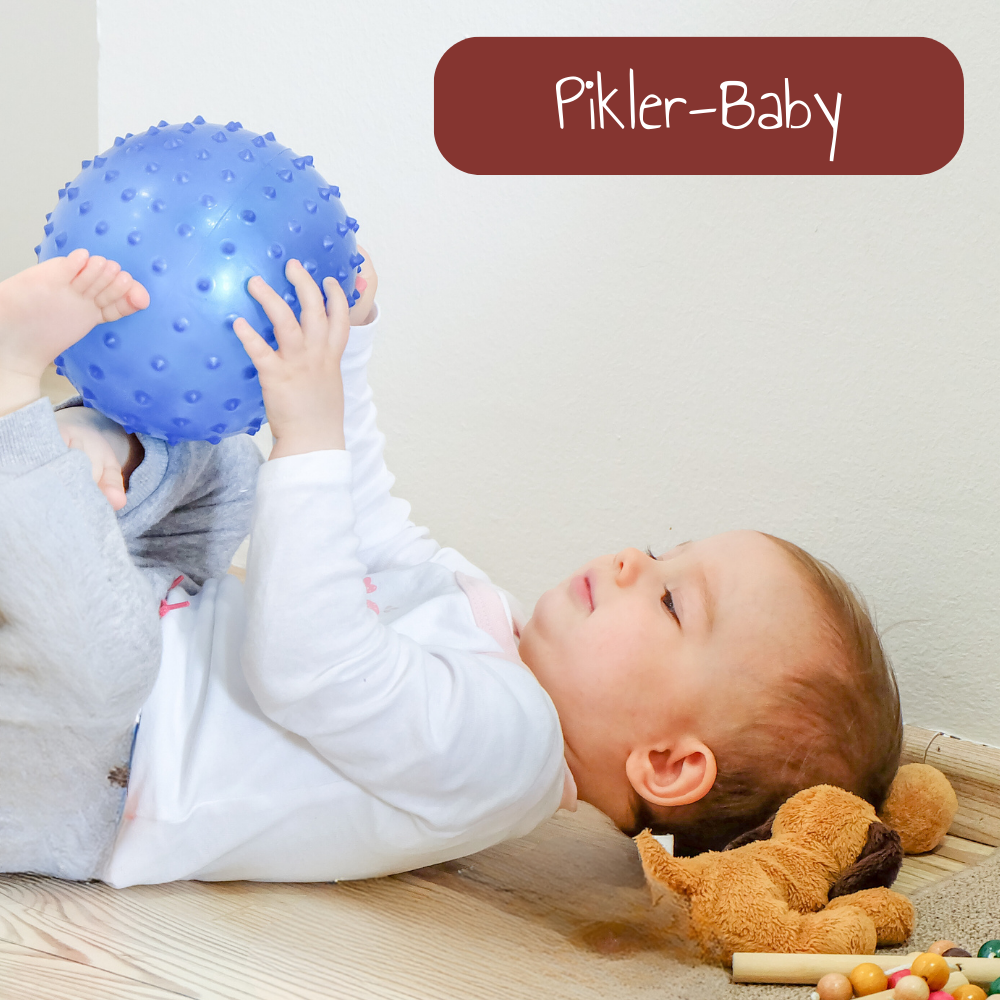 Baby liegt am Rücken und spielt mit Ball