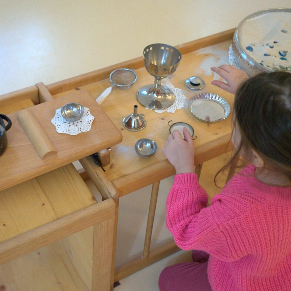 Mädchen spielt mit kleinen Metallgefäßen und Sand